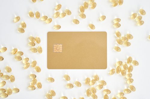Minimalist gold credit card surrounded by vitamin capsules on white background